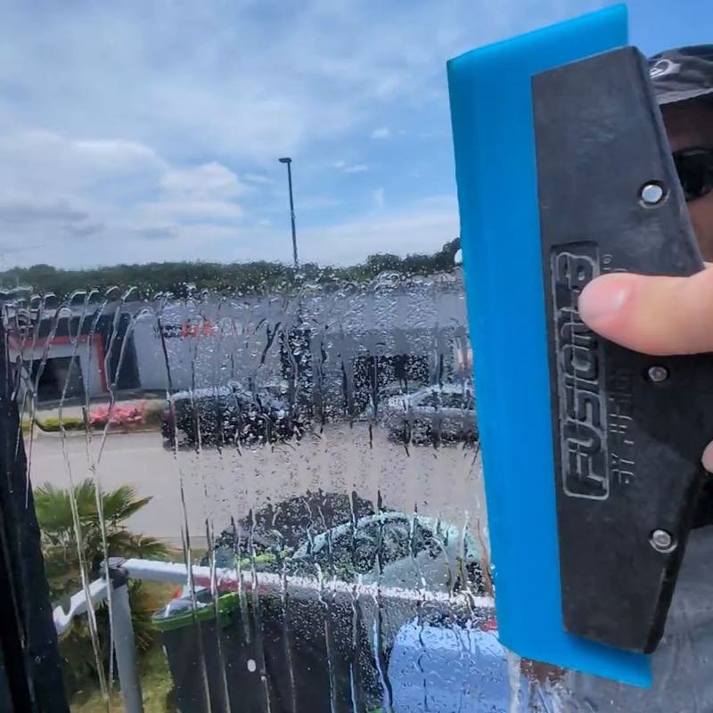 Marouffage d'un film pour vitrage à la raclette, l'eau de pose chassée vers le bord