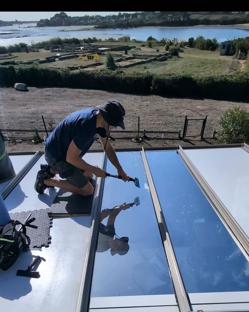 Jérôme Zielinski posant un film solaire à la raclette sur une verrière de toiture, face à la mer