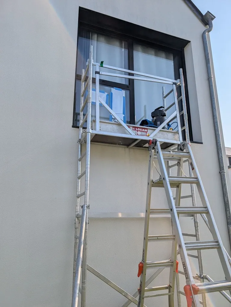 Pose de film solaire en extérieur sur une fenêtre d'étage depuis un échafaudage roulant, Morbihan